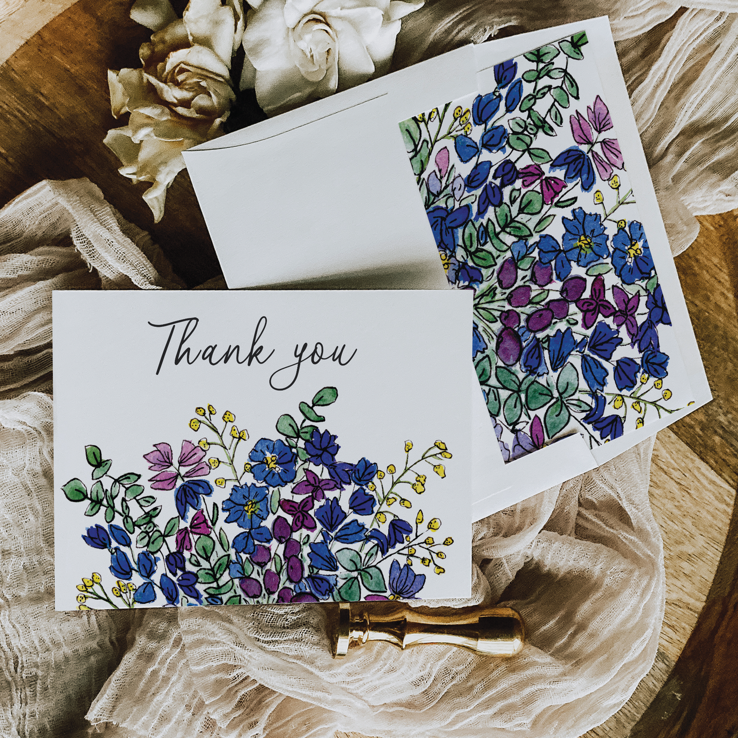 Beautiful thank you card and envelope with blue wildflowers painted in watercolors and the scripted words "Thank you" across the top of the card.